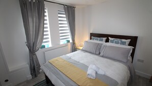 Un letto rifatto con cura, coperto da una coperta a righe e con una coperta gialla e un asciugamano arrotolato.