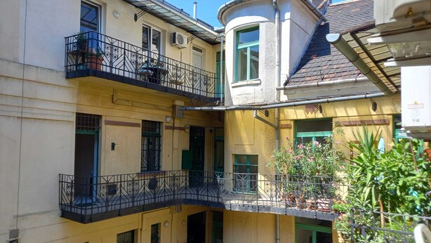 Un immeuble à plusieurs étages, doté de balcons, de portes vertes et de plantes en pot.