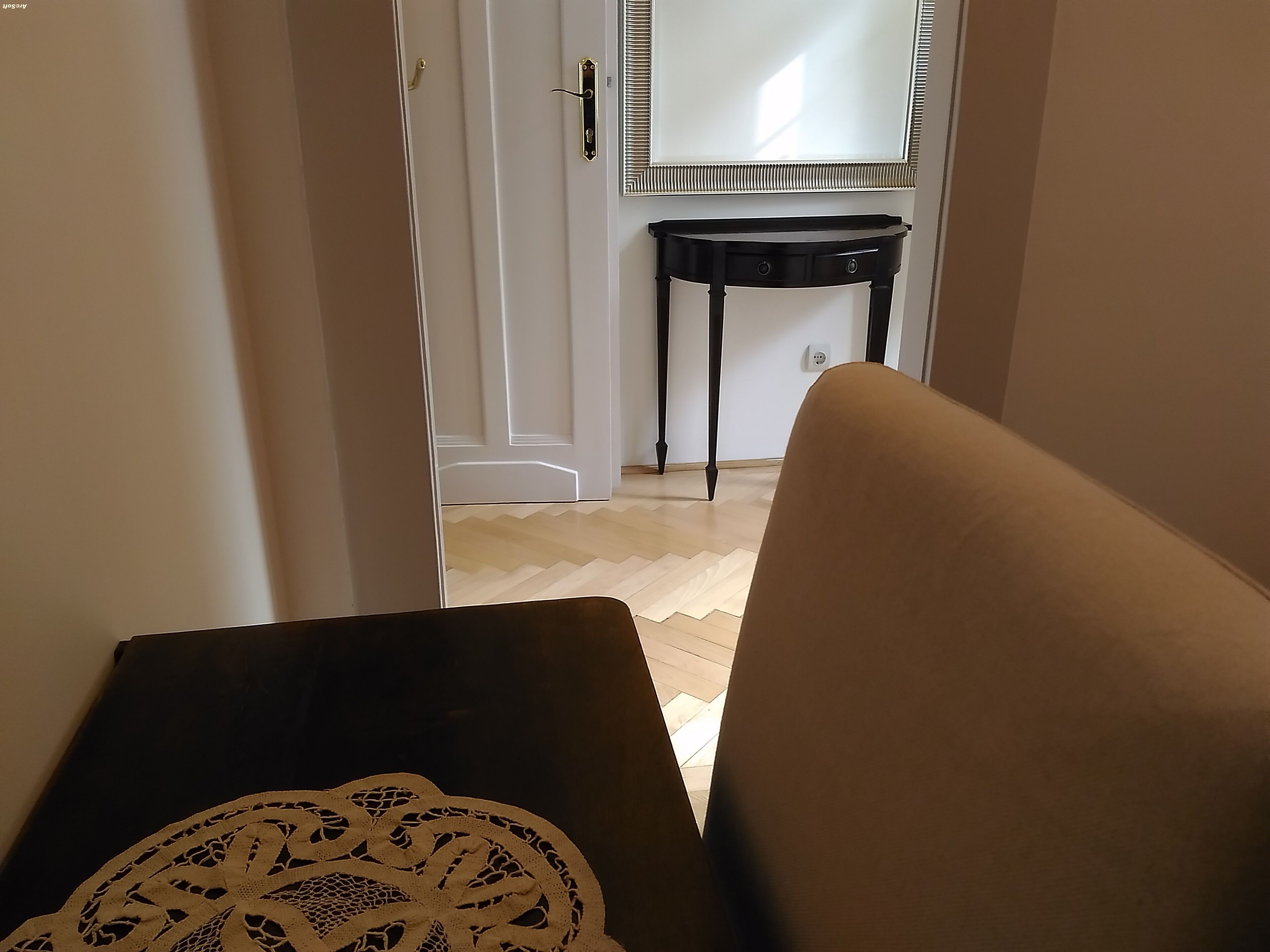 Una habitación con una puerta que da a un pasillo, un elegante escritorio consola negro y un espejo en la pared.