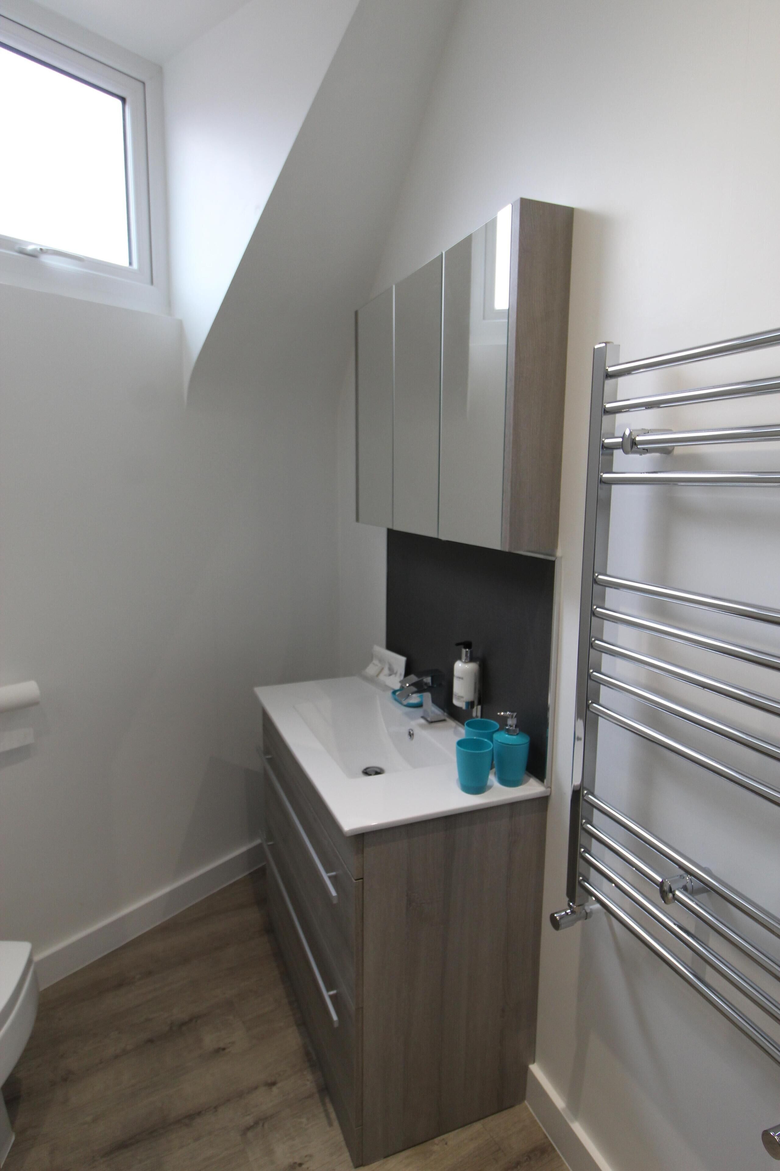 Ein modernes Badezimmer mit einem weißen Waschbecken, Holzschränken und einem Handtuchhalter.