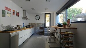Et moderne køkken med hvide skabe, en stenvæg som detalje, et ur og udsigt til det fri gennem et stort vindue.