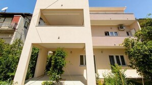 Un edificio moderno de dos pisos con techo plano, un balcón en el nivel superior y un pequeño jardín frontal.