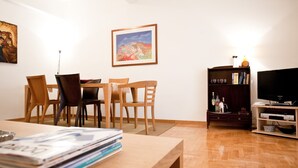 A dining area with wooden chairs and a table, a bookshelf with books and a television, and a painting on the wall. - Acropolis area next Metro & Museum (Athina)