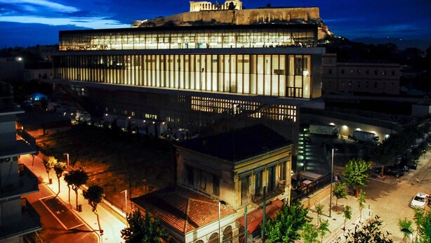 A modern building with large windows and a flat roof, surrounded by trees and a street. - Acropolis area next Metro & Museum (Athina)