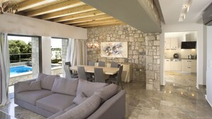 A modern living room with a stone wall, a dining area, and a kitchen. - Villa Passithea , 3 bedroom villa plus studio with private heated pool (Lindos)