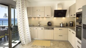 A modern kitchen with a view of the sea, featuring stainless steel appliances, light wood cabinets, and a large window with a curtain. - Villa Passithea , 3 bedroom villa plus studio with private heated pool (Lindos)