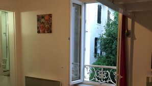 Een kamer met houten vloer, een radiator, een raam met rood gordijn, en een klein balkon met metalen hekwerk.