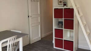 Een kamer met een wit bureau, een witte stoel, een witte bank en een rode en witte boekenkast, met een witte ladder tegen een muur.