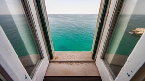A view from a window with a clear view of the ocean and a rocky outcrop. - Superior Apartment Sea View (Polignano A Mare)