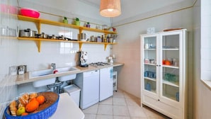 A kitchen with white cabinets, a built-in oven, a sink, and a dish rack. There are shelves above the counter holding various kitchen items. - Superior Apartment Sea View (Polignano A Mare)