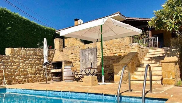 Una piscina con un muro de piedra y un patio cubierto.