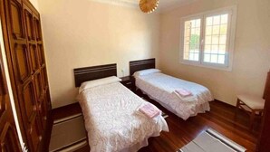 Una habitación con dos camas individuales, un armario de madera, una ventana con vistas y un ventilador de techo.