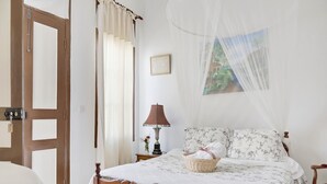 Ein Schlafzimmer mit einem hölzernen Bett, floralem Bettzeug, einem Nachttisch mit Lampe und einem Moskitonetz über dem Bett.