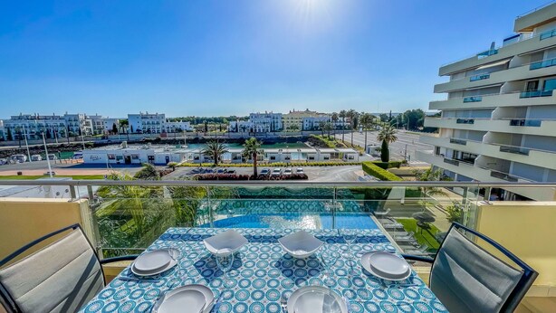 A balcony with a pool table, dining set, and a view of a coastal area with buildings.