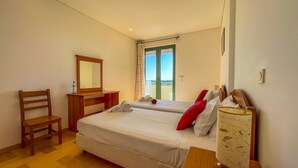 A hotel room with two beds, a wooden desk, a chair, a mirror, and a window with a view.