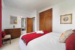 A bedroom with a bed, a dresser, a mirror, and wooden wardrobes.