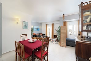 A dining area with a table set for two, a sofa, and a cabinet with dishes.