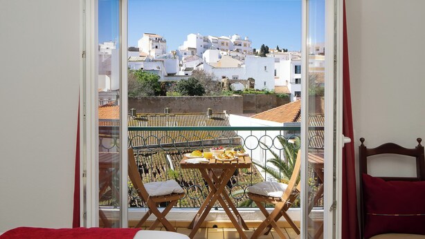 A balcony with a table and chairs, a bed, and a view of buildings. - (^ ‿ ^) Cozy & Bright, near the Beach, Marina, Historic Center and Supermarket (Lagos)