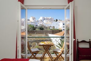 A balcony with a table and chairs, a bed, and a view of buildings.