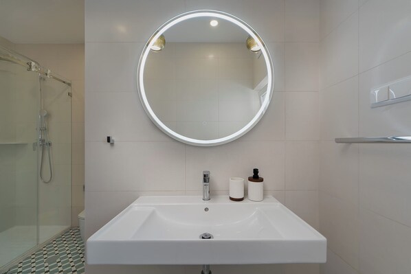 Une salle de bain moderne avec un miroir rond, un lavabo blanc et un espace douche.
