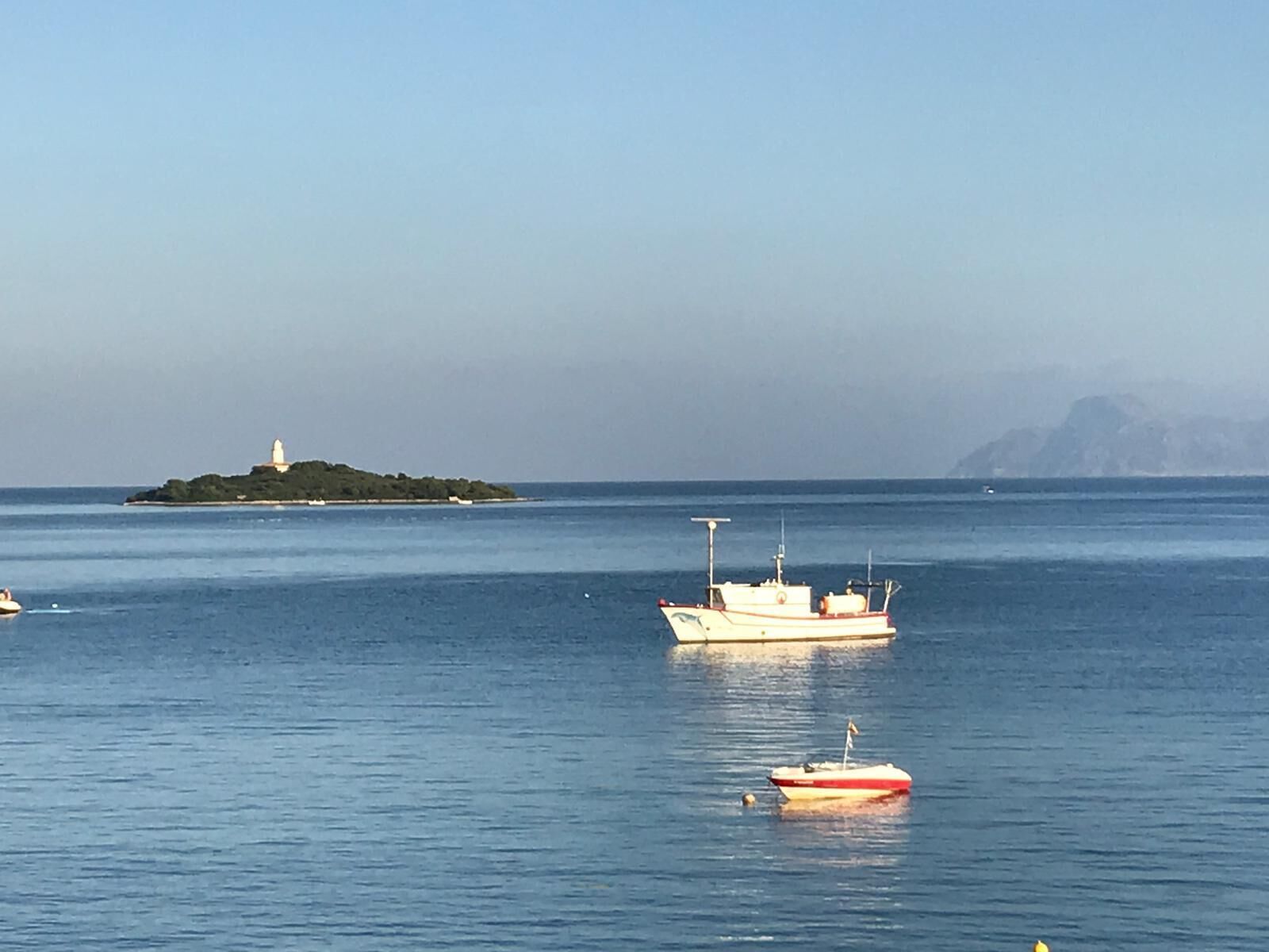 Une mer calme, avec une petite île à l’horizon et un bateau ancré près du rivage.