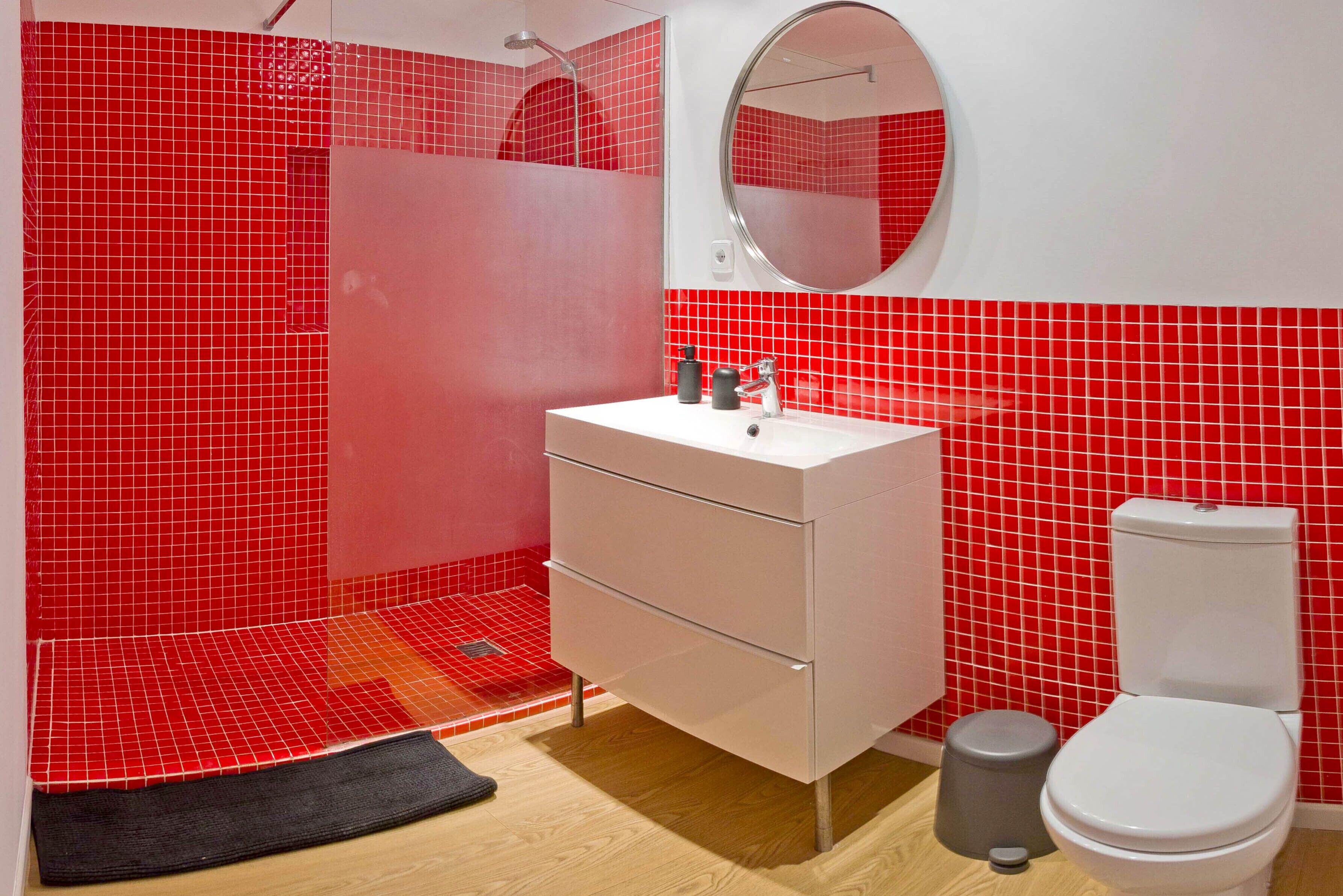 A bathroom with a white sink, a mirror, and a toilet against a red tiled wall.