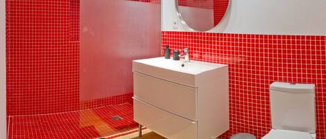 A bathroom with a white sink, a mirror, and a toilet against a red tiled wall.