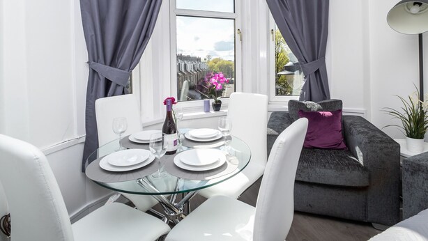 A dining area with a glass table, white chairs, and a view of the city through a window. - One Bedroom Apartment by Klass Living Serviced Accommodation Rutherglen - Crossroads Apartment With WiFi and Parking (Glasgow)