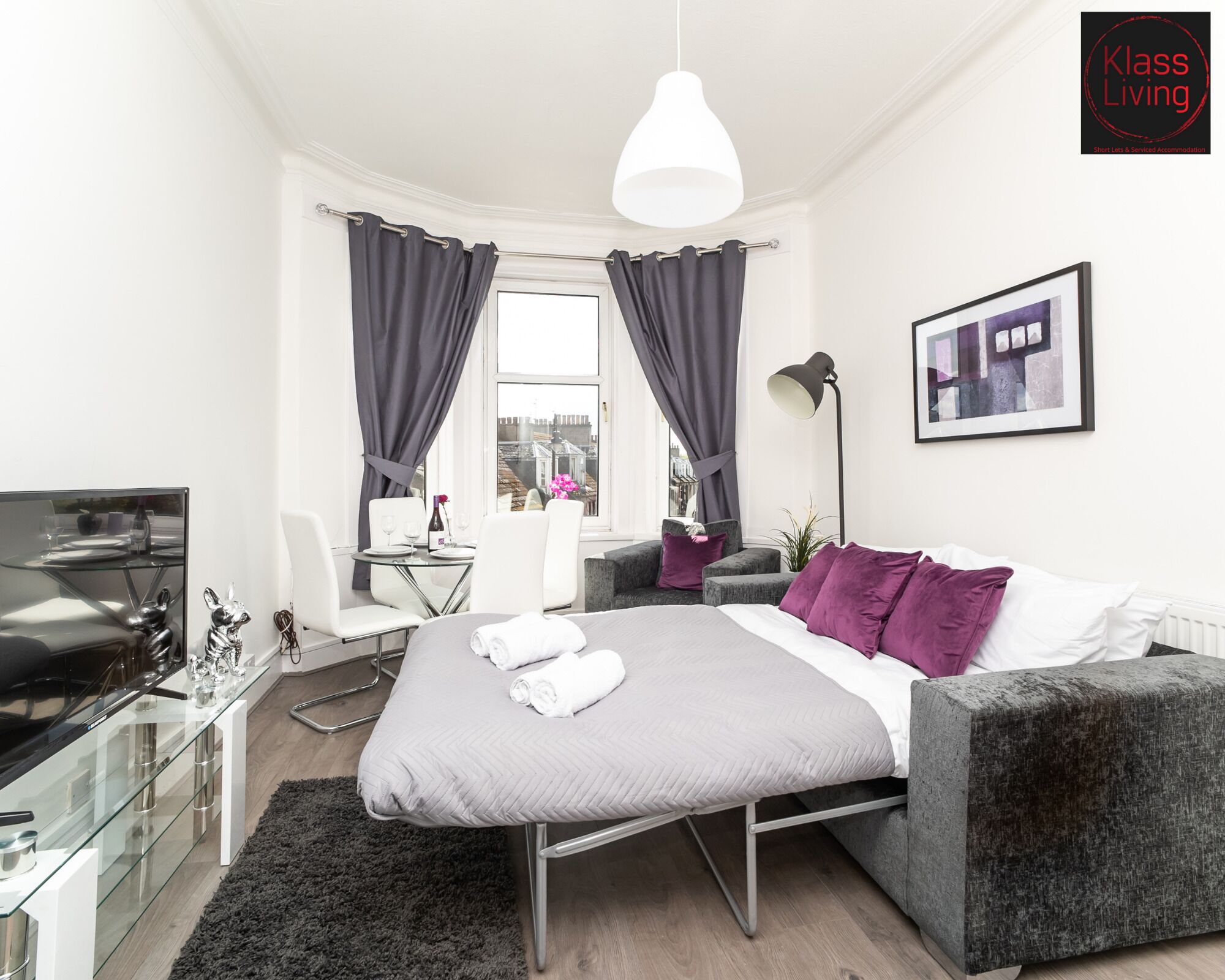 Quarto de hotel moderno com cama, escrivaninha, cadeira, televisão e janela com cortinas.