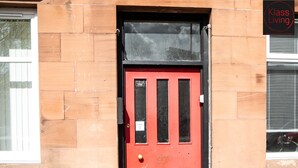 A red door with a sign above it, a window to the left, and a sign to the right. - One Bedroom Apartment by Klass Living Serviced Accommodation Rutherglen - Crossroads Apartment With WiFi and Parking (Glasgow)