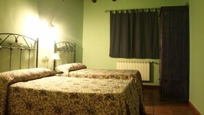 A room with two beds, a radiator, a window with curtains, and a wooden ceiling.