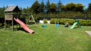 A playground with a wooden playhouse, red and green slides, and a small blue car.