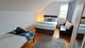 A bedroom with two single beds, a sofa, a small table, and a window with curtains.