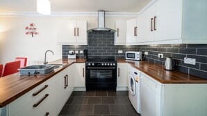 A modern kitchen with white cabinets, a black stove, a microwave, and a washing machine.