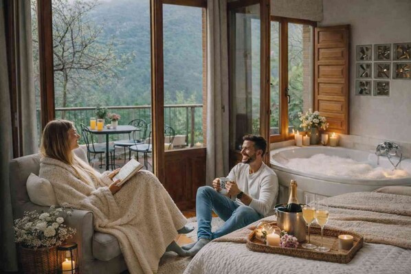 A couple relaxing by a window with a view of the outdoors, a bathtub, and a tray with drinks and candles.
