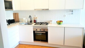 Ett kompakt kök med vita skåp, en gasspis, en inbyggd ugn och en mikrovågsugn placerad ovanför spisen.
