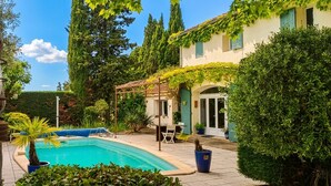 Une piscine agrémentée d’une pergola, d’un espace salon couvert et d’un bâtiment doté d’un toit en tuiles.