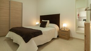 A bedroom with a bed, bedside tables, a nightstand, a wooden wardrobe, and a mirror. - Apartment in Arrecife 101- 5 PEOPLE (Arrecife)