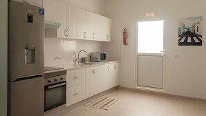 A modern kitchen with white cabinets, a stainless steel refrigerator, a microwave, and a stove.