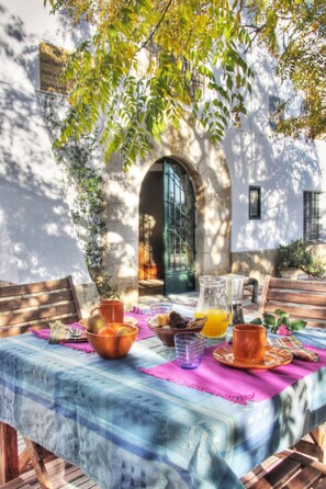 A table set with breakfast items, a pitcher, and a glass of orange juice, with a view of a building and a tree in the background. - Catalan farmhouse with pool and an incredible natural environment, for groups of 7 or 13 (Bescanó)