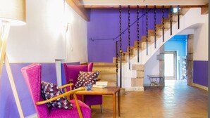 Une pièce avec un mur violet, un escalier en bois et une chaise avec un coussin à carreaux.