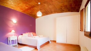 Une chambre avec deux lits, une armoire blanche, un plafond en briques et un mur violet.