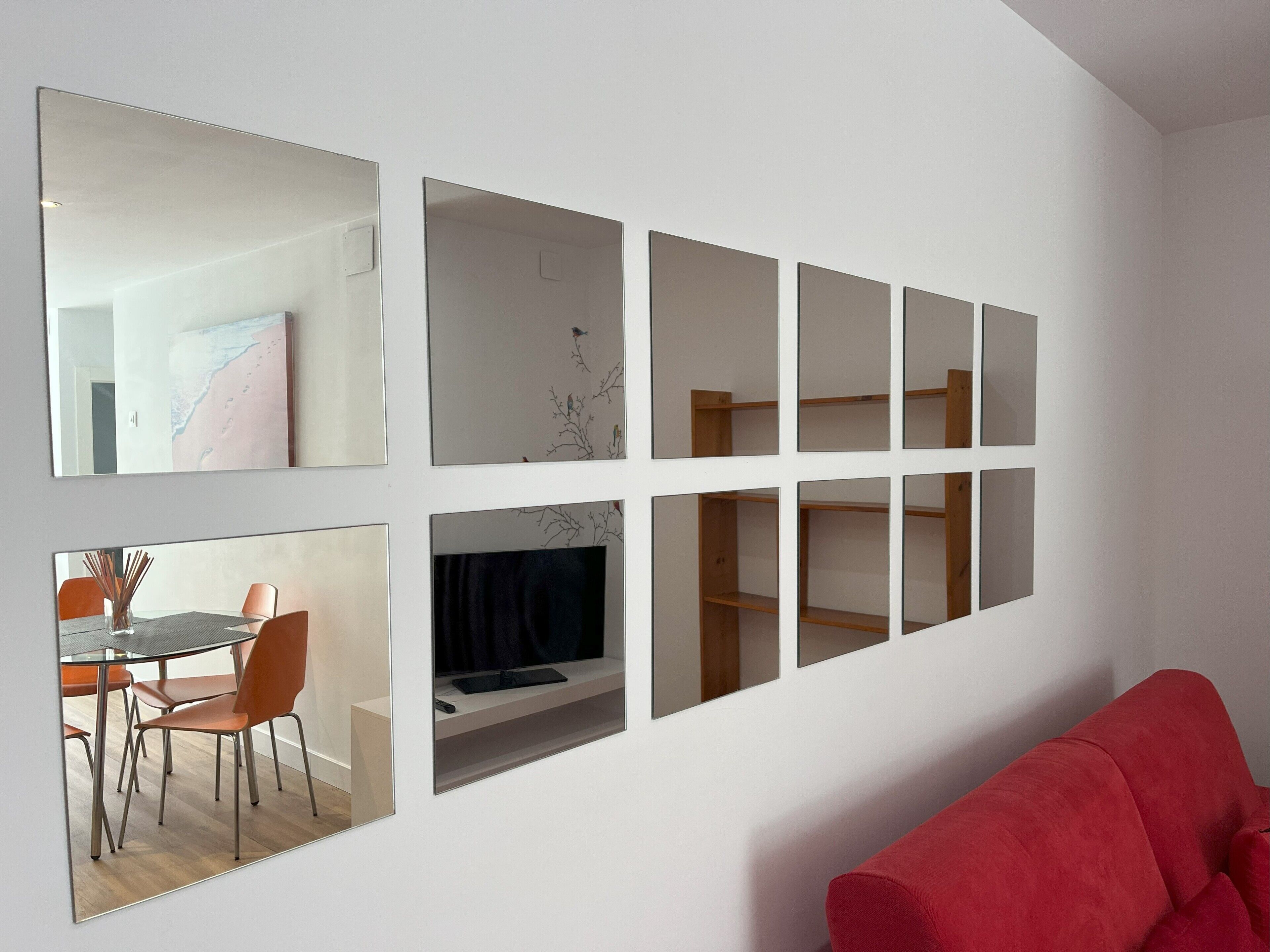 A modern living room with a red sofa, a dining area with a glass table and chairs, and a wall with multiple mirrors and shelves.