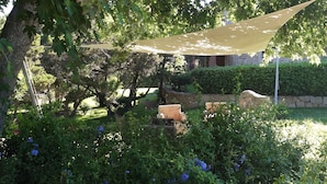 Un jardin doté d’un espace de repos ombragé, d’un mur en pierre et d’une végétation luxuriante.