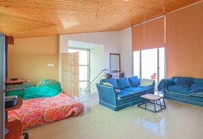 Amplia sala de estar con techo de madera, un juego de sofá, una cama con colcha de colores y una escalera que conduce a un nivel superior.