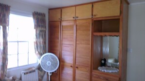 A room with a wooden wardrobe, a radiator, and a standing fan.