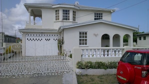 A two-story house with a white exterior, a balcony with a white balustrade, and a red car parked in front.