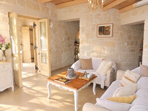 A cozy living room with a stone wall, a wooden coffee table, a white sofa, and a chandelier. - A charming 3 bedroom stone villa w/ privacy, private pool & fantastic sea views. (Chania)