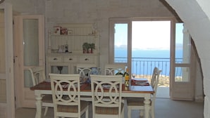 Un coin repas avec une table et des chaises, une vue sur la mer et un mur en pierre.