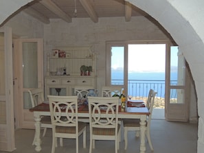 A dining area with a table and chairs, a view of the sea, and a stone wall.